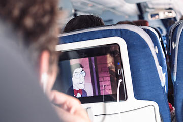 Image showing Reflection of a passenger on an airplane touch screen monitor while watching cartoon during long flight. Entertainment service system in aircraft.