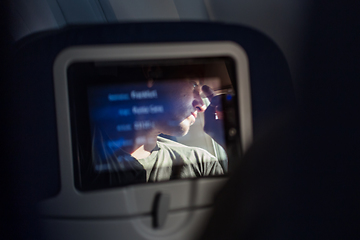 Image showing Reflection of a passenger on an airplane touch screen monitor during long flight. Entertainment service system in aircraft.