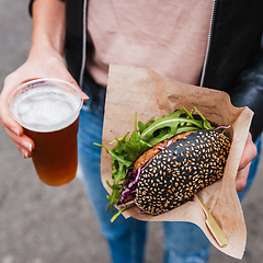 Image showing Close up of woman hands holding delicious organic salmon vegetarian burger and homebrewed IPA beer on open air beer an burger urban street food festival in Ljubljana, Slovenia.