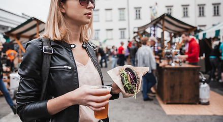 Image showing Close up of woman hands holding delicious organic salmon vegetarian burger and homebrewed IPA beer on open air beer an burger urban street food festival in Ljubljana, Slovenia.