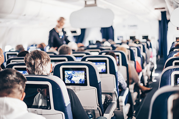 Image showing Interior of airplane with passengers on seats and stewardess in uniform walking the aisle, serving people. Commercial economy flight service concept.