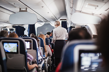 Image showing Interior of airplane with passengers on seats and stewardess in uniform walking the aisle, serving people. Commercial economy flight service concept.