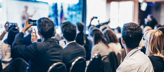 Image showing Speaker giving a talk in conference hall at business event. Rear view of unrecognizable people in audience at the conference hall. Business and entrepreneurship concept.