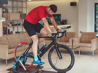 Image showing A man riding a triathlon bike on a machine simulation in a modern living room. Training during pandemic conditions.