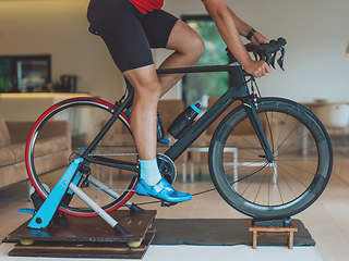 Image showing A man riding a triathlon bike on a machine simulation in a modern living room. Training during pandemic conditions.