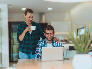 Image showing A young married couple is talking to parents, family and friends on a video call via a laptop while sitting in the living room of their modern house