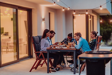 Image showing A group of young diverse people having dinner on the terrace of a modern house in the evening. Fun for friends and family. Celebration of holidays, weddings with barbecue.