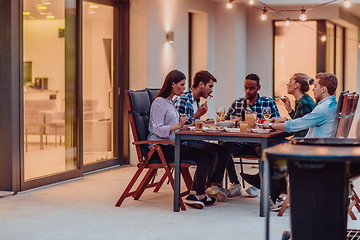 Image showing A group of young diverse people having dinner on the terrace of a modern house in the evening. Fun for friends and family. Celebration of holidays, weddings with barbecue.