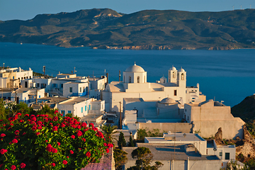 Image showing View of Plaka village on Milos island over red geranium flowers on sunset in Greece