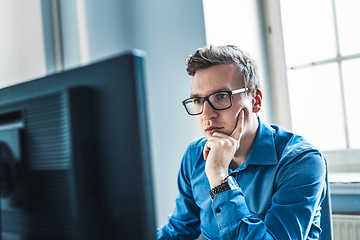 Image showing Handsome Young Businessman Wearing Eyeglasses Sitting at his Table Inside the Office, Looking at the Report on his Computer Screen.