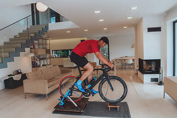 Image showing A man riding a triathlon bike on a machine simulation in a modern living room. Training during pandemic conditions.