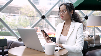 Image showing A busy businesswoman using laptop and having coffee