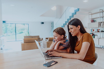Image showing Mother with her daughter talking on laptop with family and friends while sitting in modern living room of big house