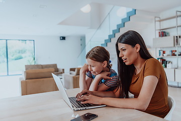 Image showing Mother with her daughter talking on laptop with family and friends while sitting in modern living room of big house