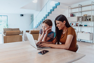 Image showing Mother with her daughter talking on laptop with family and friends while sitting in modern living room of big house