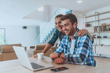 Image showing A young married couple is talking to parents, family and friends on a video call via a laptop while sitting in the living room of their modern house