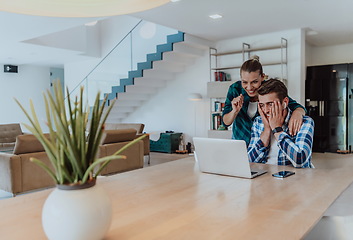 Image showing A young married couple is talking to parents, family and friends on a video call via a laptop while sitting in the living room of their modern house