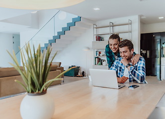 Image showing A young married couple is talking to parents, family and friends on a video call via a laptop while sitting in the living room of their modern house