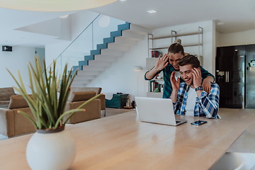 Image showing A young married couple is talking to parents, family and friends on a video call via a laptop while sitting in the living room of their modern house