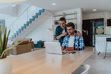 Image showing A young married couple is talking to parents, family and friends on a video call via a laptop while sitting in the living room of their modern house