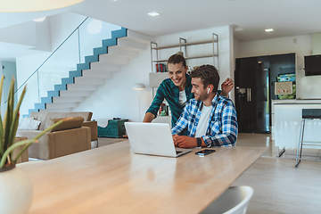 Image showing A young married couple is talking to parents, family and friends on a video call via a laptop while sitting in the living room of their modern house