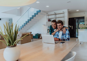 Image showing A young married couple is talking to parents, family and friends on a video call via a laptop while sitting in the living room of their modern house