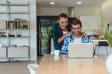 Image showing A young married couple is talking to parents, family and friends on a video call via a laptop while sitting in the living room of their modern house