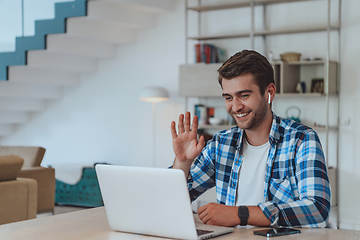 Image showing The man sitting at a table in a modern living room, with headphones using a laptop for business video chat, conversation with friends and entertainment