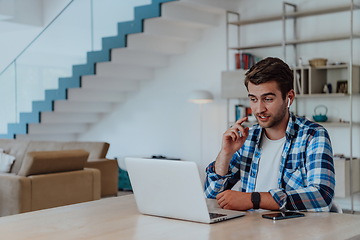 Image showing The man sitting at a table in a modern living room, with headphones using a laptop for business video chat, conversation with friends and entertainment