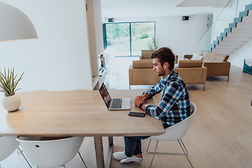 Image showing The man sitting at a table in a modern living room, with headphones using a laptop for business video chat, conversation with friends and entertainment