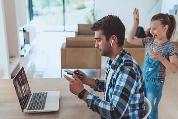 Image showing The man sitting at a table in a modern living room, with headphones using a laptop and smartphone for business video chat, conversation with friends and entertainment