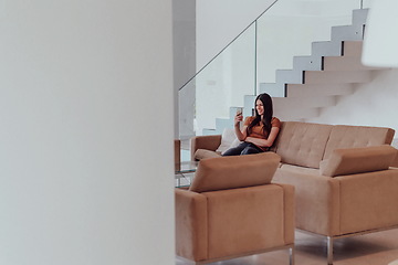 Image showing Woman using smartphone for video call while sitting in modern house