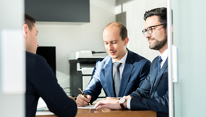 Image showing Group of confident successful business people reviewing and signing a contract to seal the deal at business meeting in modern corporate office.