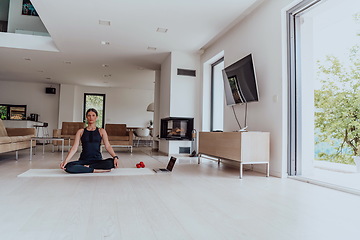 Image showing Young Beautiful Female Exercising, Stretching and Practising Yoga with Trainer via Video Call Conference in Bright Sunny House. Healthy Lifestyle, Wellbeing and Mindfulness Concept.