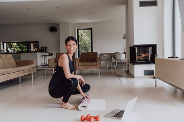 Image showing A young woman in sports clothes preparing sports equipment for online training in her living room