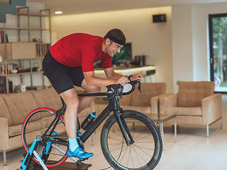 Image showing A man riding a triathlon bike on a machine simulation in a modern living room. Training during pandemic conditions.