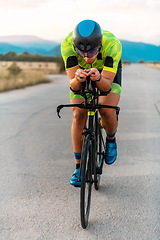 Image showing Triathlete riding his bicycle during sunset, preparing for a marathon. The warm colors of the sky provide a beautiful backdrop for his determined and focused effort.