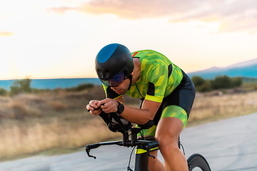 Image showing Triathlete riding his bicycle during sunset, preparing for a marathon. The warm colors of the sky provide a beautiful backdrop for his determined and focused effort.