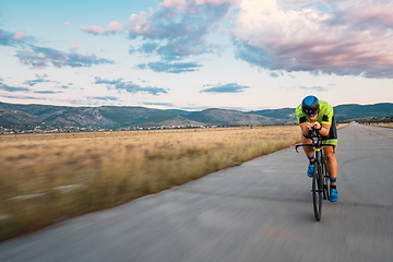 Image showing Triathlete riding his bicycle during sunset, preparing for a marathon. The warm colors of the sky provide a beautiful backdrop for his determined and focused effort.