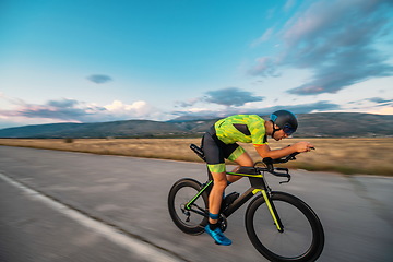 Image showing Triathlete riding his bicycle during sunset, preparing for a marathon. The warm colors of the sky provide a beautiful backdrop for his determined and focused effort.