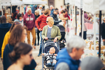 Image showing Mother waling and pushing his infant baby boy child in stroller in crowd of unrecognizable people wisiting sunday flea market in Malaga, Spain.