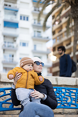 Image showing Young mother with her cute infant baby boy child on bench in city park.