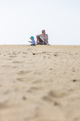 Image showing Mother playing his infant baby boy son on sandy beach enjoying summer vacationson on Lanzarote island, Spain. Family travel and vacations concept.