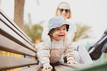 Image showing Young mother with her cute infant baby boy child on bench on urban children's playground on warm summer day.