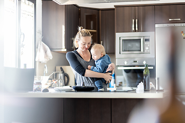 Image showing Happy mother and little infant baby boy making pancakes for breakfast together in domestic kitchen. Family, lifestyle, domestic life, food, healthy eating and people concept.