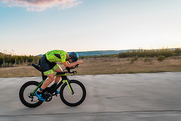 Image showing Triathlete riding his bicycle during sunset, preparing for a marathon. The warm colors of the sky provide a beautiful backdrop for his determined and focused effort.