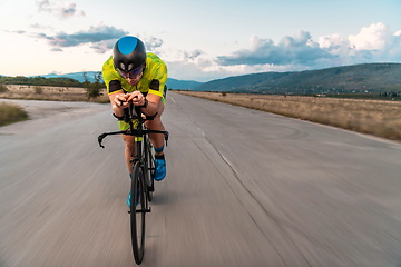 Image showing Triathlete riding his bicycle during sunset, preparing for a marathon. The warm colors of the sky provide a beautiful backdrop for his determined and focused effort.