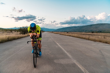 Image showing Triathlete riding his bicycle during sunset, preparing for a marathon. The warm colors of the sky provide a beautiful backdrop for his determined and focused effort.