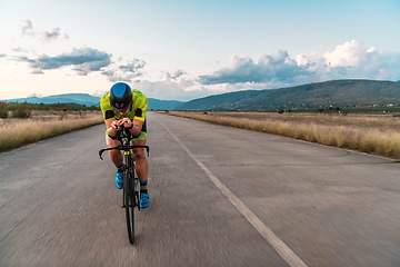 Image showing Triathlete riding his bicycle during sunset, preparing for a marathon. The warm colors of the sky provide a beautiful backdrop for his determined and focused effort.