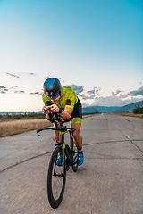 Image showing Triathlete riding his bicycle during sunset, preparing for a marathon. The warm colors of the sky provide a beautiful backdrop for his determined and focused effort.